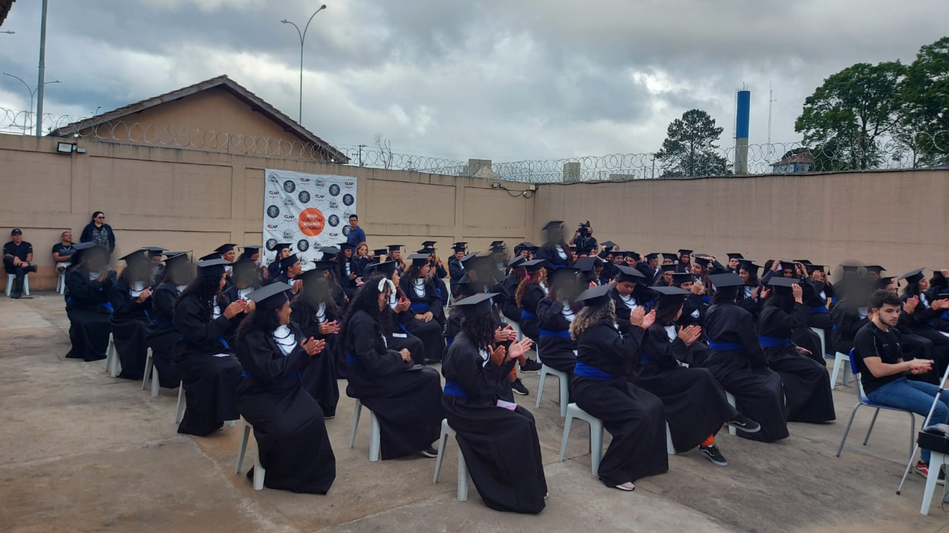 84 formandas do CIS usando becas. Elas estão sentadas em cadeiras