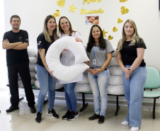 um homem de roupas pretas e quatro mulheres. Duas delas seguram uma almofada de amamentação branca