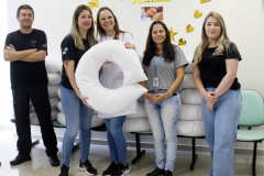 um homem de roupas pretas e quatro mulheres. Duas delas seguram uma almofada de amamentação branca