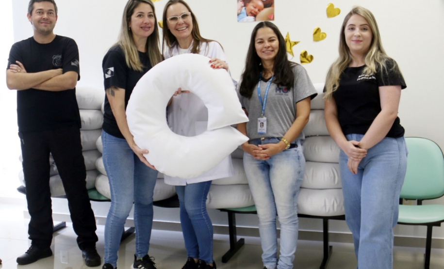 um homem de roupas pretas e quatro mulheres. Duas delas seguram uma almofada de amamentação branca