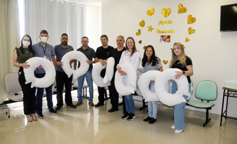 nove pessoas, homens e mulheres, seguram seis almofadas brancas de amamentação