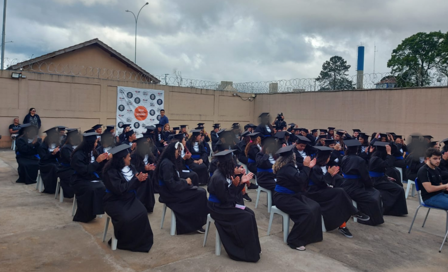 84 formandas do CIS usando becas. Elas estão sentadas em cadeiras